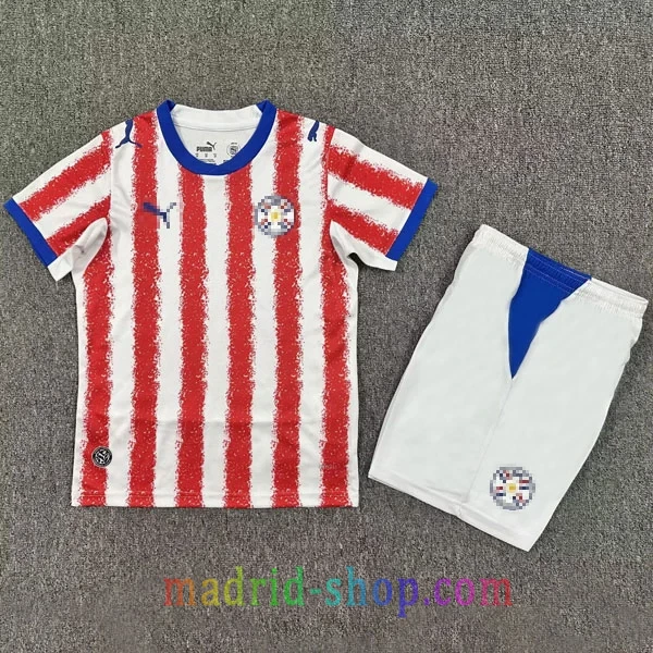 Camiseta Paraguay Primera Equipación 2026 Niño Camiseta Paraguay Primera Equipación 2026 Niño con franjas rojas tierra colorada y pantalón corto.